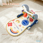 A baby activity gym mat with a wheeled base, shown on a white faux-fur rug with overlaid dimension lines and text indicating size measurements. The mat is cream with blue, yellow, red, and multicolor printed graphics and text, including a rainbow, flowers, hearts, and a blue circle reading 'peace'.