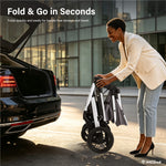 A woman in a cream blazer and light blue jeans is folding a compact rolling suitcase with a telescoping handle and black wheels next to an open black car trunk in an outdoor urban setting. Text at the top reads 'Fold & Go in Seconds' and a small 'IMLSved' logo appears in the bottom right corner.